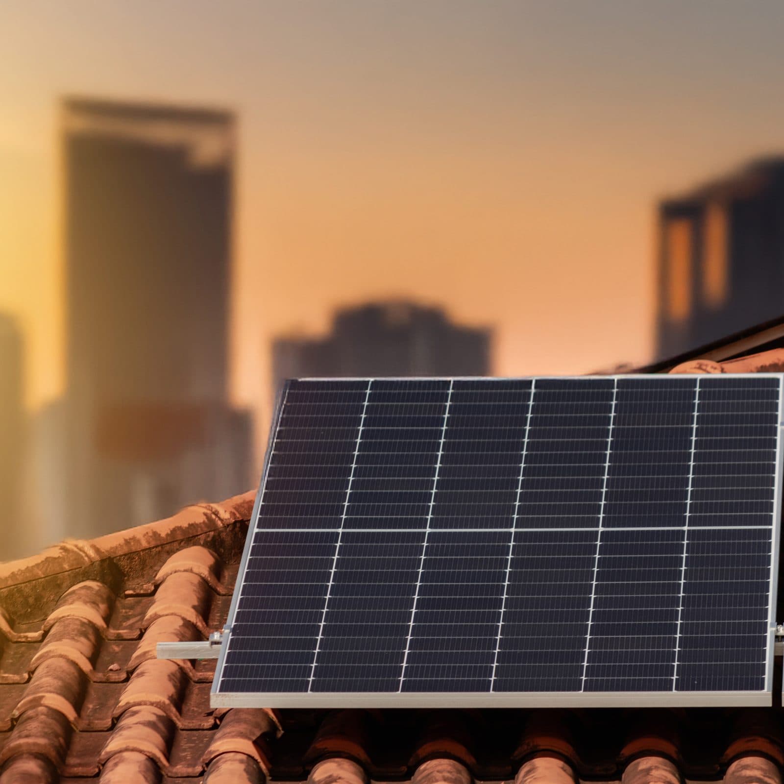 Solar panels on a tiled roof at sunset with a city skyline behind
