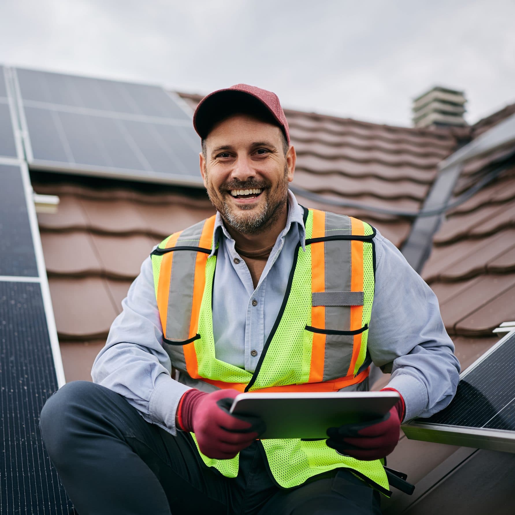 Smiling solar installer sitting on a roof beside newly fitted panels
